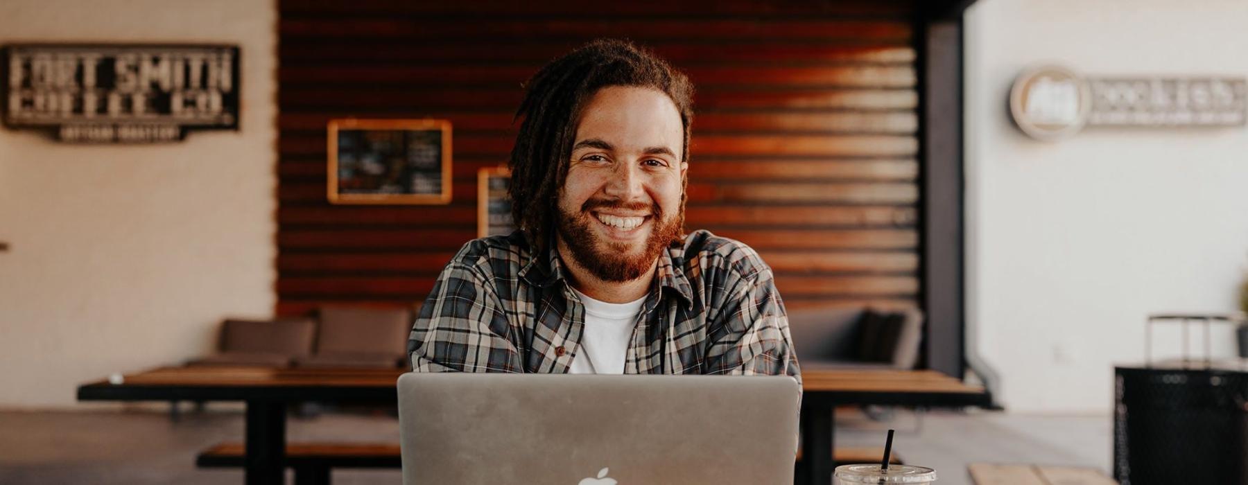 man sits with a drink in front of an open laptop in local restaurant